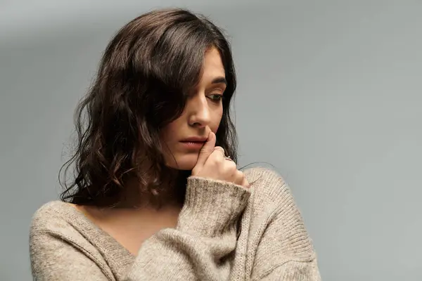 Brunette woman in casual attire ponders thoughtfully against a soft grey backdrop. — Stock Photo