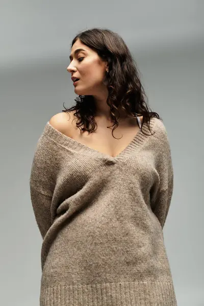 Embracing beauty in a cozy beige sweater on a serene grey backdrop. — Stock Photo