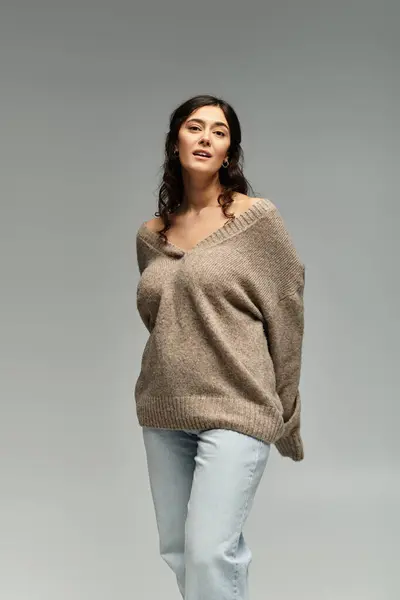 Embracing beauty and confidence in a cozy beige sweater on a soft grey backdrop. — Stock Photo