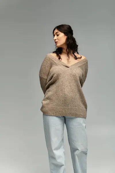 Beautiful young plus size woman in cozy beige sweater poses elegantly in studio. — Stock Photo