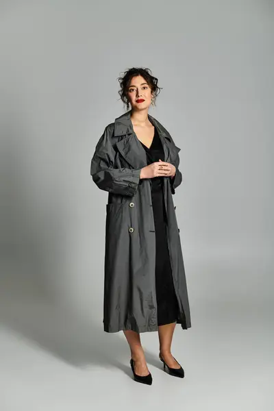 Bruna donna in elegante abbigliamento posa con grazia in studio impostazione su sfondo grigio. — Foto stock