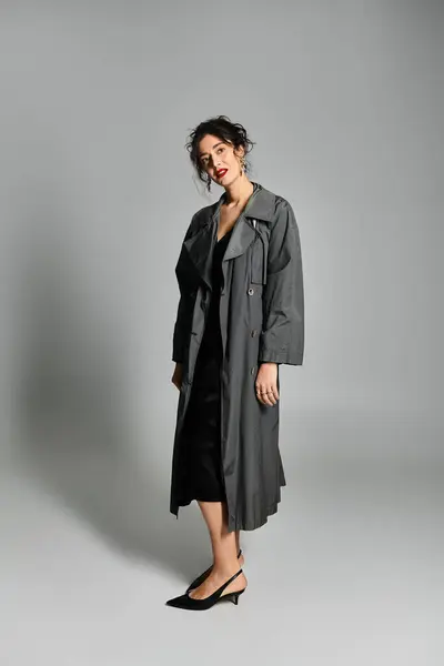 Elegante donna bruna in abbigliamento chic posa con grazia su uno sfondo grigio. — Foto stock