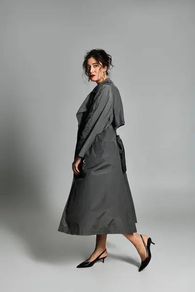 Elegante donna bruna posa con grazia in un ambiente di studio con sfondo grigio. — Foto stock