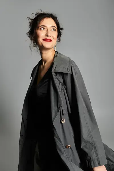 Elegante donna bruna posa con grazia in elegante abbigliamento contro uno sfondo grigio. — Foto stock