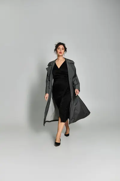 Elegante donna bruna in elegante abbigliamento monolocale su sfondo grigio. — Foto stock
