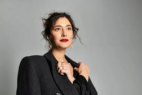 Elegant brunette woman in chic attire posing gracefully against a simple grey background. — Stock Photo