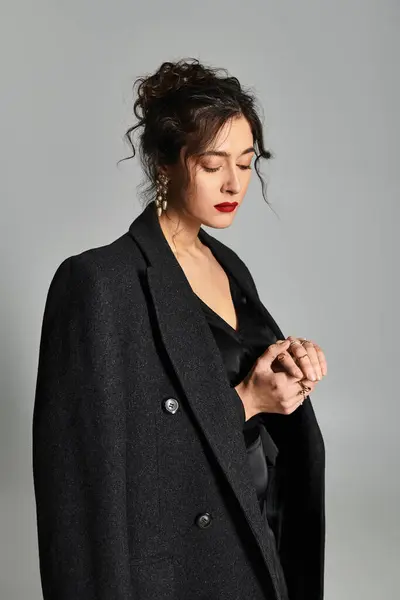 Brunette woman in elegant black attire poses gracefully against a grey backdrop. — Stock Photo