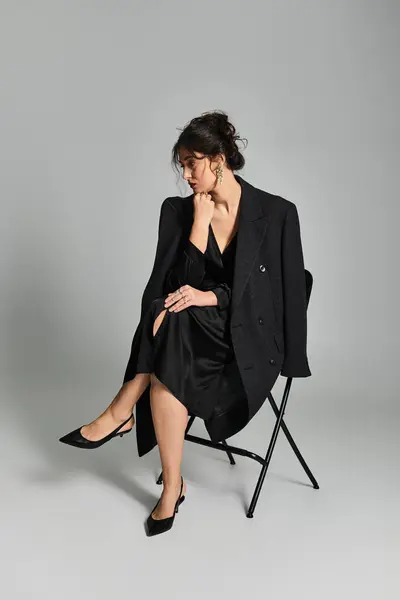 Elegante morena sentada en estudio sobre fondo gris con elegante atuendo. - foto de stock