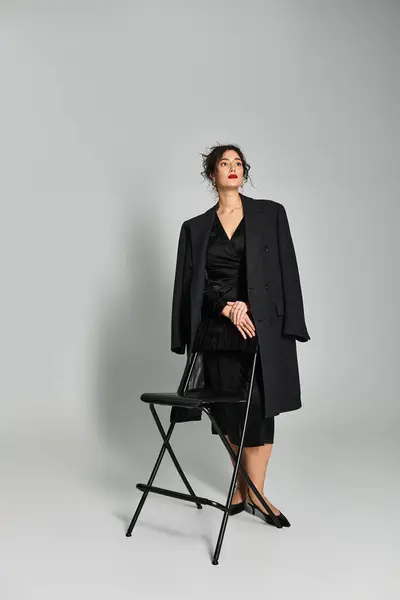 A brunette in elegant attire poses gracefully against a grey backdrop. — Stock Photo