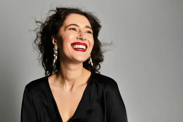 Elegant brunette woman radiating joy in a stylish studio setting with grey background. — Stock Photo
