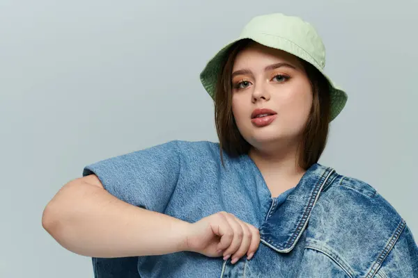 Plus size beauty confidently poses in a denim outfit with a trendy bucket hat capturing attention. — Stock Photo
