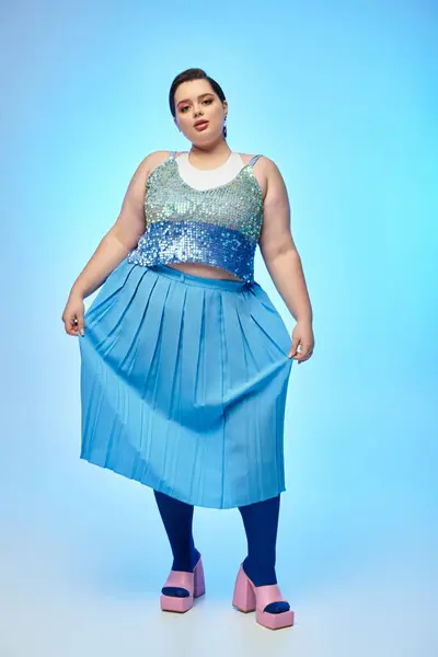 Eine selbstbewusste Plus-Size-Frau glänzt in einem funkelnden Outfit vor leuchtend blauem Hintergrund. — Stockfoto