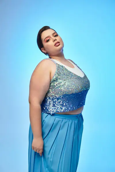 A confident young woman showcases her beauty in a vibrant blue atmosphere wearing sparkly attire. — Stock Photo