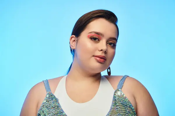 Una giovane donna plus size mette in mostra la sua bellezza con un trucco audace su uno sfondo blu. — Foto stock