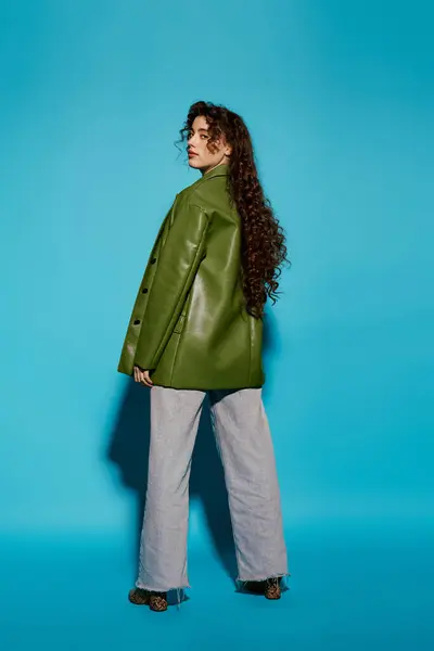 Jeune femme présente une veste verte tendance, style exubérant et confiance contre un mur bleu audacieux. — Photo de stock