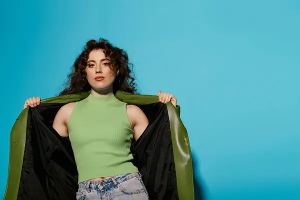 A beautiful young woman showcases her chic green top and stylish jacket under bright light. — Stock Photo