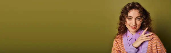 A young woman with curly hair smiles brightly, flaunting her fashion against a green wall. — Stock Photo