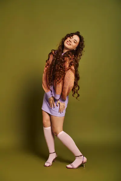 A stylish young woman playfully showcases her colorful outfit against a green backdrop. — Stock Photo