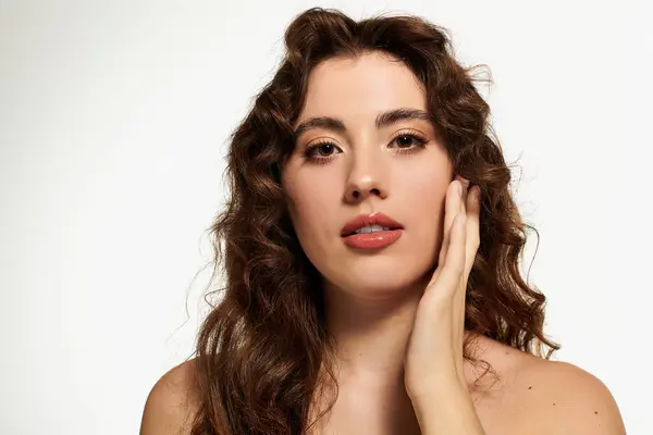 Charming young woman with beautiful curls gently touching her face in a serene studio setting — Stock Photo
