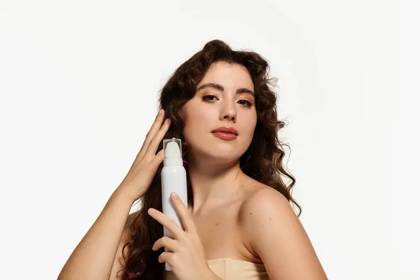 Giovane donna mette in mostra la sua routine di bellezza, mentre elegantemente in possesso di una bottiglia spray in uno spazio luminoso. — Foto stock