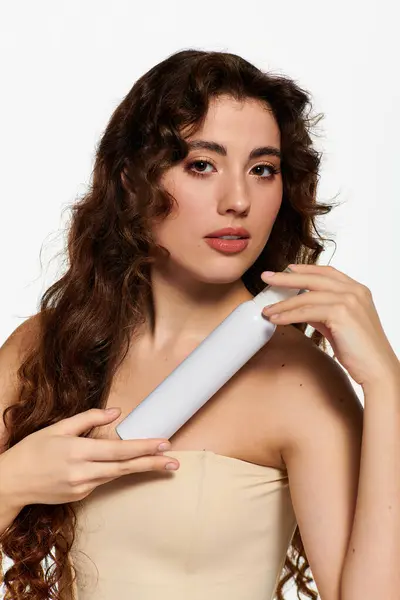 Une jeune femme pose élégamment avec un produit de beauté, rayonnant de confiance. — Photo de stock