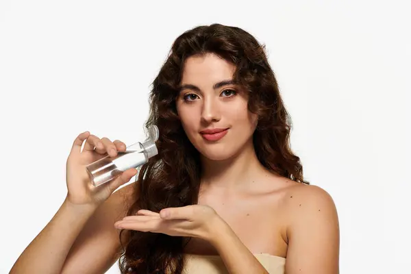 Young woman with beautiful hair demonstrates a skincare product in a bright studio space. — Stock Photo