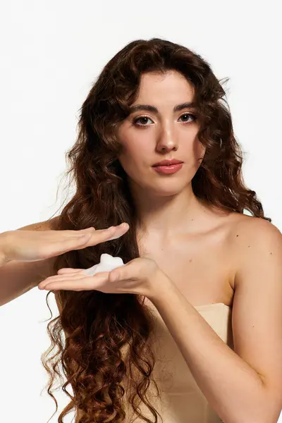 A beautiful young woman showcases a skincare product with elegant poise in a bright studio. — Stock Photo