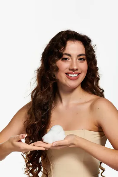 Young woman with curly hair smiles while playfully holding fluffy foam in her hands. — Stock Photo