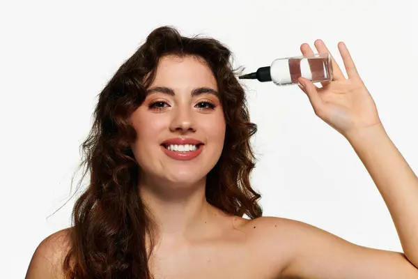 In a bright studio, a stylish woman smiles as she applies hair beauty product. — Stock Photo
