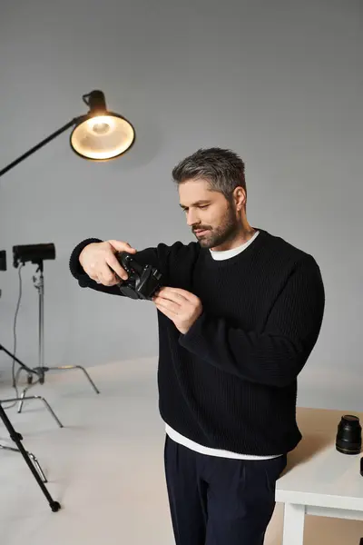 A focused man adjusts his camera gear in a studio, getting ready for a shoot. — Stock Photo