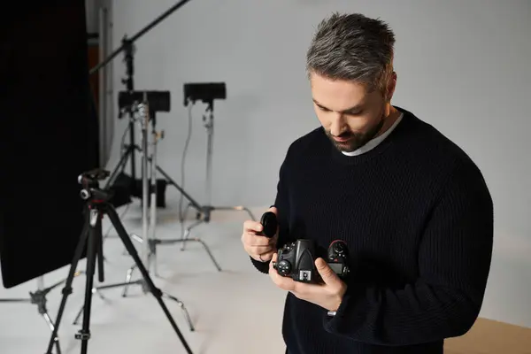 A dedicated man carefully tweaks his camera settings in an organized photography studio. — стоковое фото