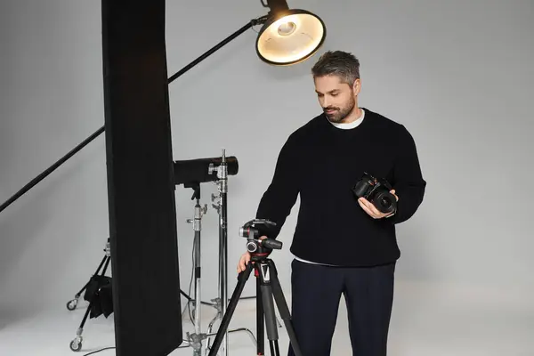 Un hombre instala cuidadosamente su cámara y equipo de iluminación en un estudio moderno, preparándose para una sesión de fotos. - foto de stock
