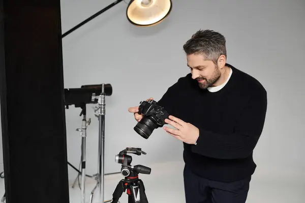 A man is focused on adjusting his camera settings while preparing for a studio shoot. — Stock Photo