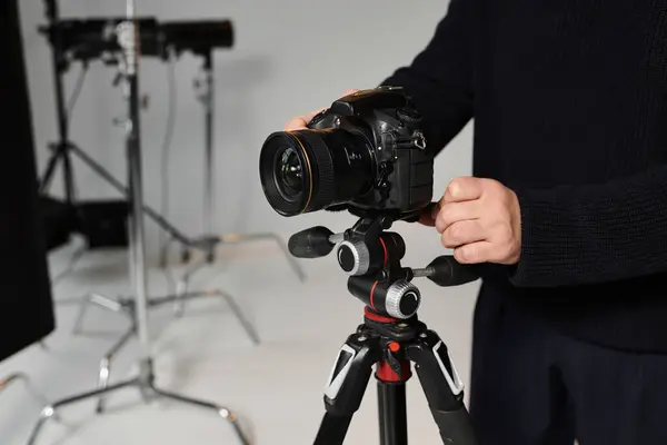 A focused man adjusts his camera on a tripod, preparing for an indoor photoshoot in the studio. — Stock Photo