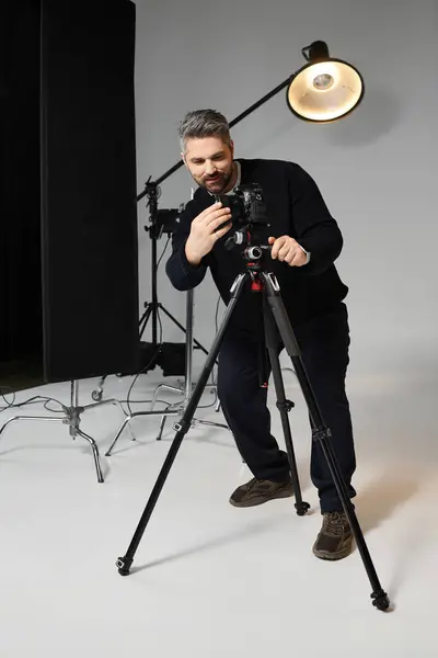 A skilled man focuses intently on his camera in a well equipped studio, preparing for a shoot. — Stock Photo