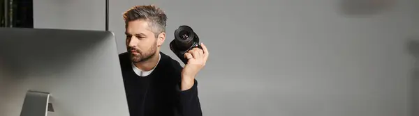 A man focused on his computer screen, holding a camera and working in a modern studio environment. — Stock Photo