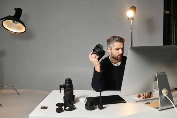 Man focuses on his editing task while holding a camera and surrounded by studio tools and lights. — Stock Photo