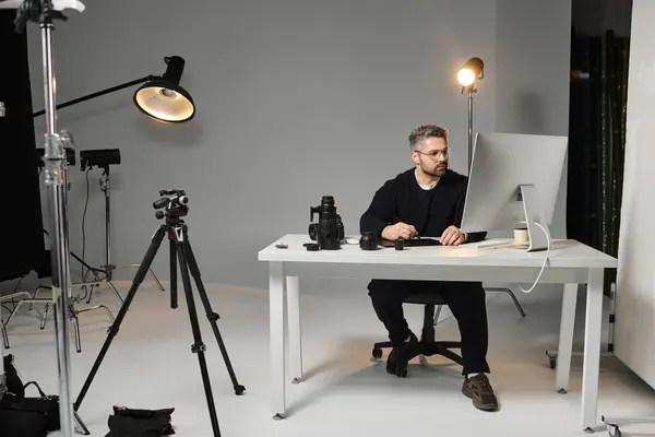 Uma pessoa dedicada trabalha duro em uma mesa em meio a equipamentos de fotografia e luzes de estúdio. — Fotografia de Stock