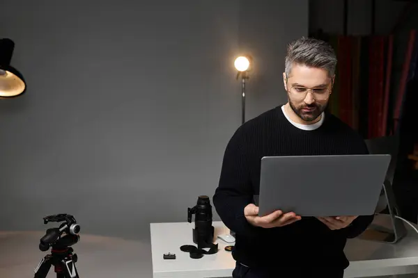 Человек напряженно работает над своим ноутбуком, редактируя изображения в стильной студии фотографии. — стоковое фото