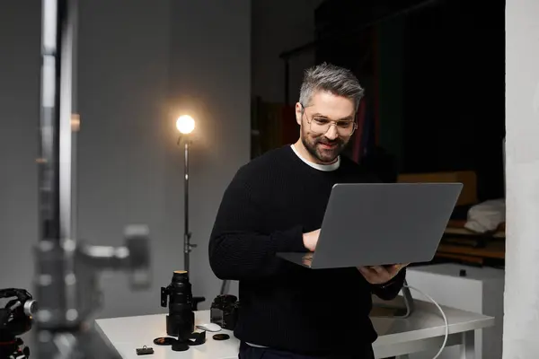 Un uomo esperto digita su un computer portatile in uno studio elegante con attrezzatura fotografica e illuminazione calda. — Foto stock