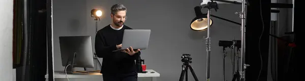 A man focuses on his laptop while surrounded by photography equipment in a modern workspace. — Stock Photo