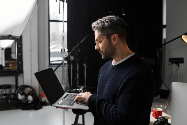Focused man engages with his laptop while surrounded by photography gear and soft lighting. — Stock Photo