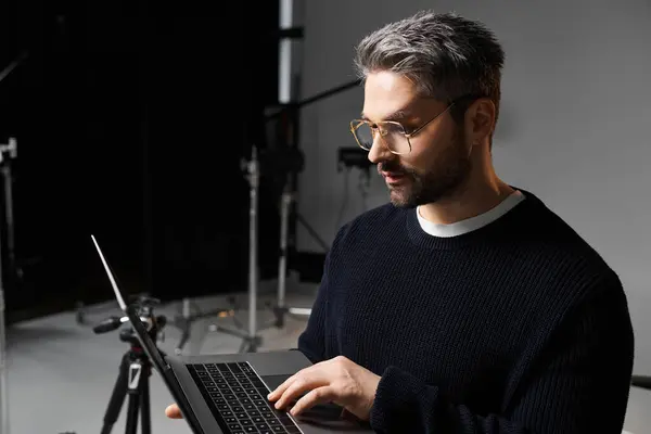 Um homem se envolve com seu laptop, concentrando-se em tarefas criativas em um ambiente de trabalho moderno. — Fotografia de Stock