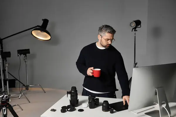 A man enjoys a warm drink while preparing his equipment in a sleek photography studio. — Stock Photo