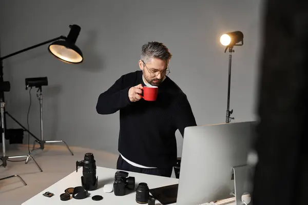 A dedicated person enjoys a warm drink at a sleek desk filled with photography gear. — Stock Photo