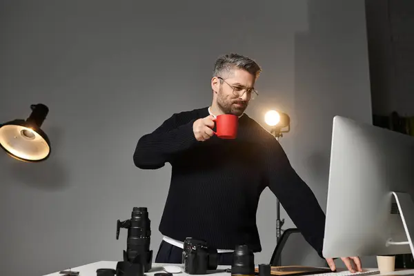 A talented man sips coffee and engages with his computer in an inspiring workspace. — Stock Photo