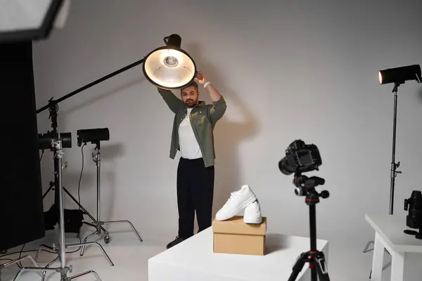 Um homem modifica habilmente a iluminação do estúdio para capturar um produto de sapato em exibição. — Fotografia de Stock