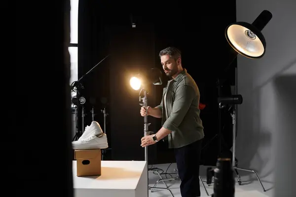 A man skillfully arranges the lighting for an attractive sneaker display in a photography studio. — Stock Photo