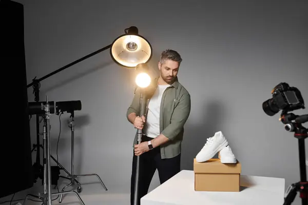 A man adjusts bright lighting equipment while showcasing stylish footwear on a pedestal. — Stock Photo
