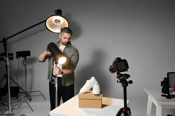 A man adjusts lighting equipment to capture the perfect shot of a sneaker on display. — Stock Photo